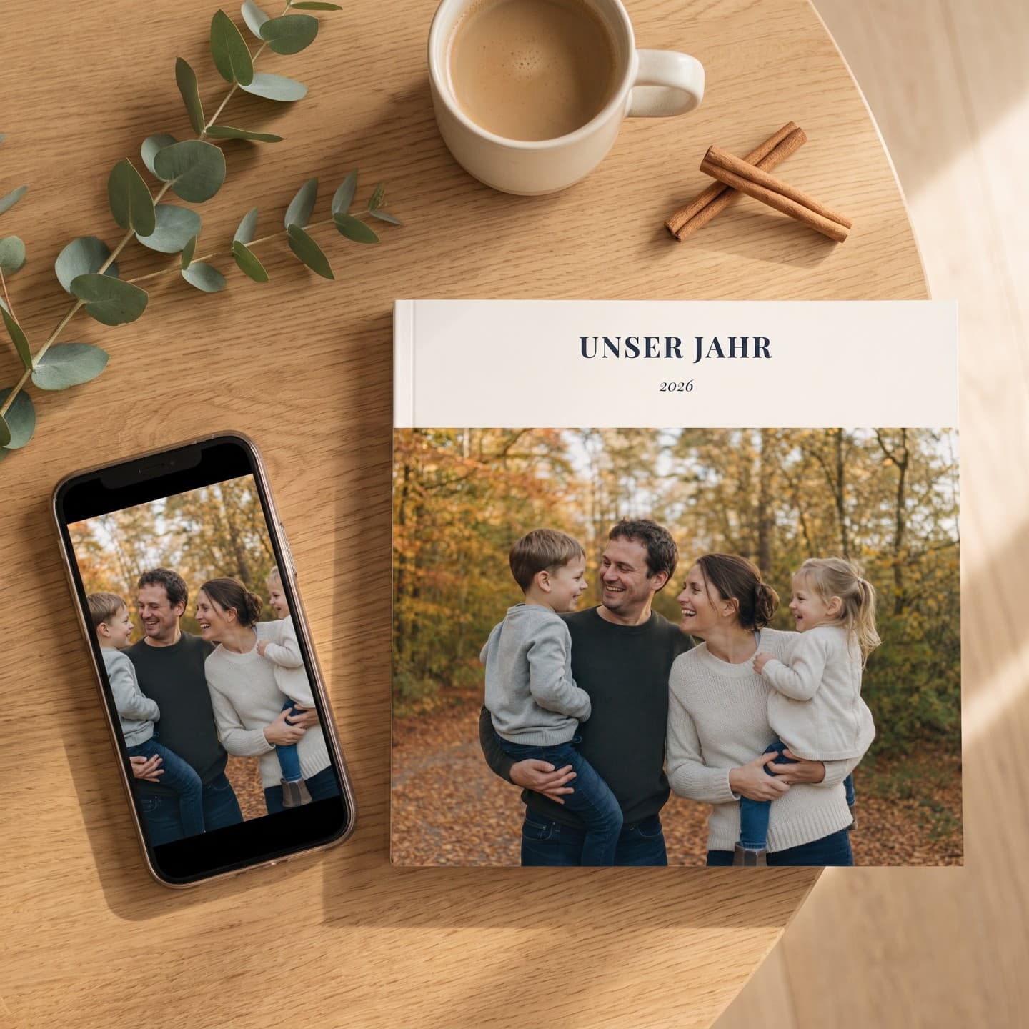 Fotobuch „Unser Jahr" auf einem Holztisch, daneben ein Handy mit demselben Foto