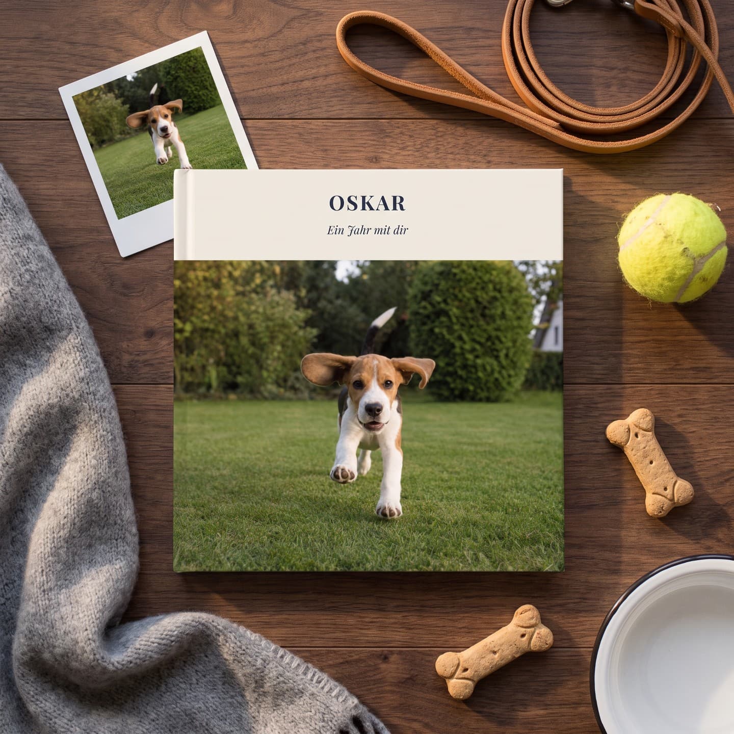 Fotoboken ”Oskar” på ett trägolv, bredvid en polaroidbild, ett koppel, en tennisboll och hundkex