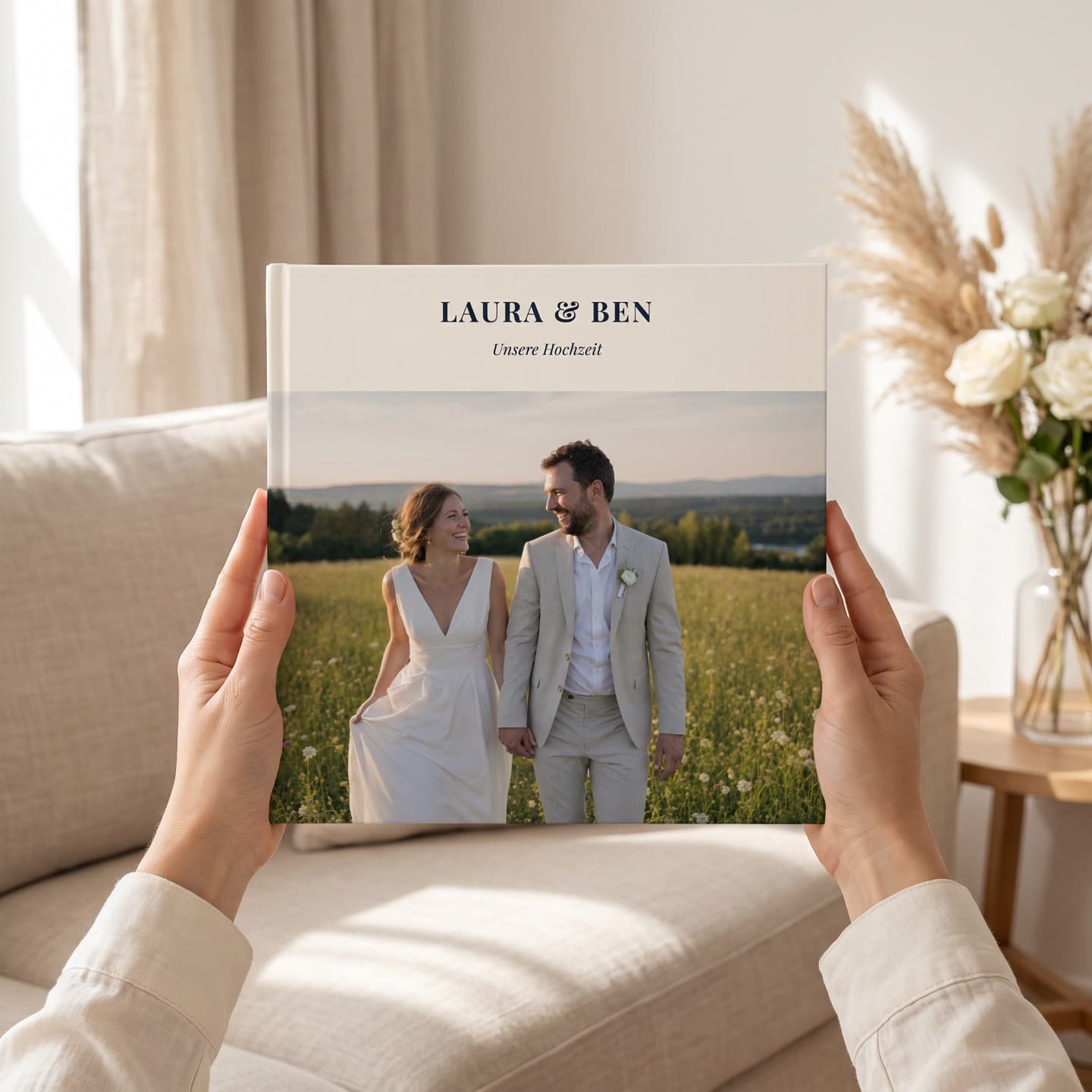 Kāzu albums „Laura & Ben“ divās rokās gaišā dzīvojamā istabā