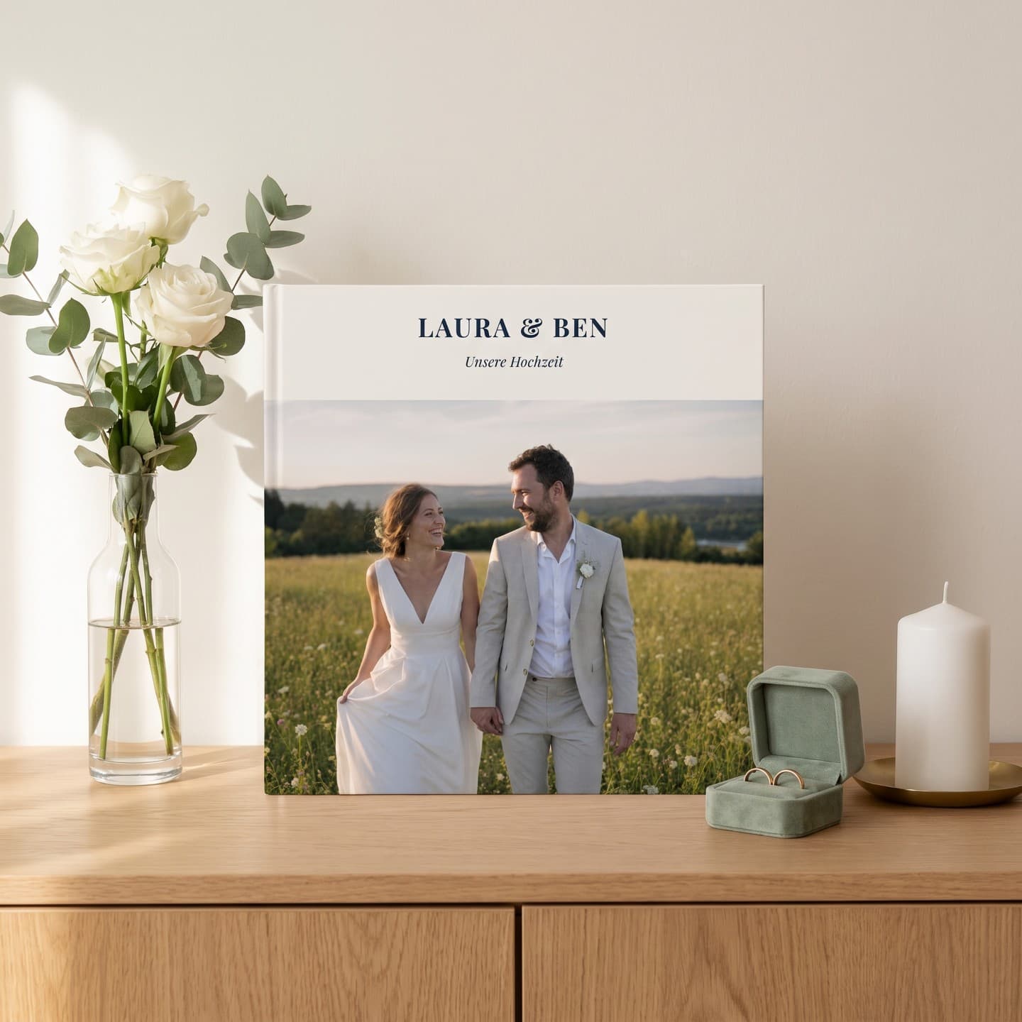 Hochzeitsalbum „Laura & Ben" auf der Kommode neben Rosen und Eheringen