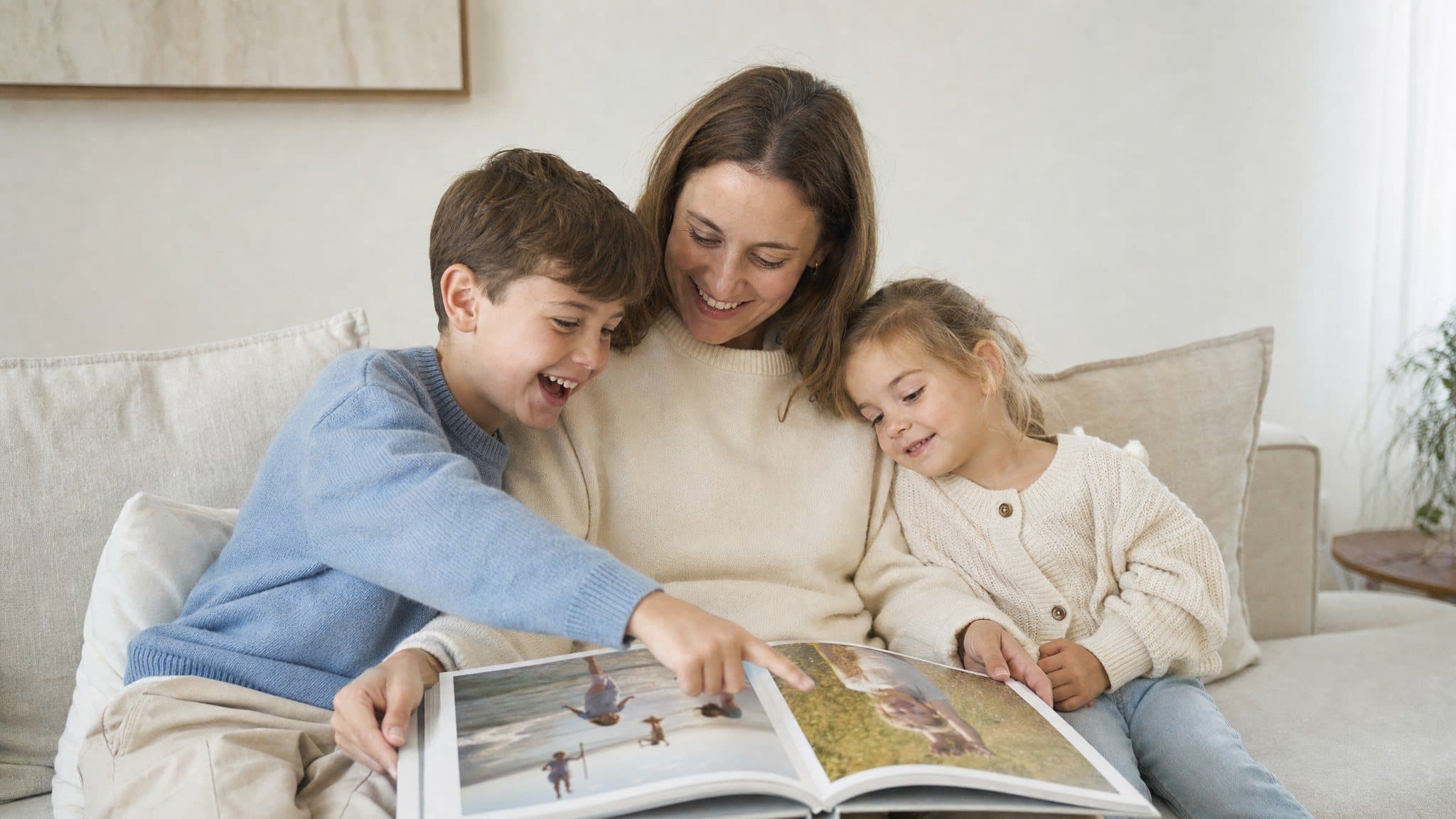 Mutter und zwei Kinder schauen auf dem Sofa lachend in ein Fotobuch